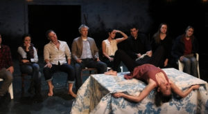 Image of Eight Actors looking embarassingly at another actor: a woman in a seagull pose splayed out on a table with her legs open