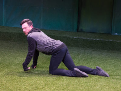 An actor walking on his hands and knees on a grass-covered stage. He is pretending to be a dog.