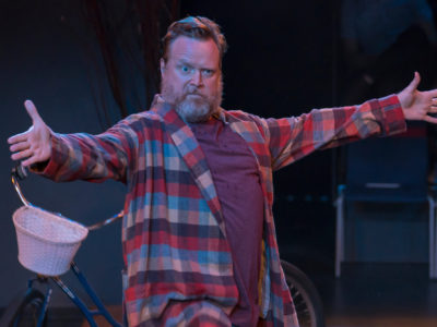 An actor in a scene: A bearded man with arms outstretched