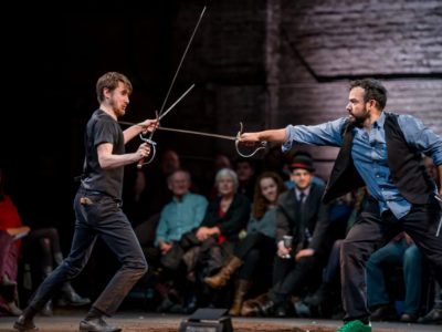Two actors sword fighting with audience in the background