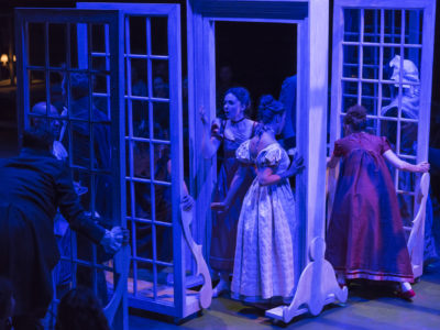 A group of actors move window frames through a darkened space.