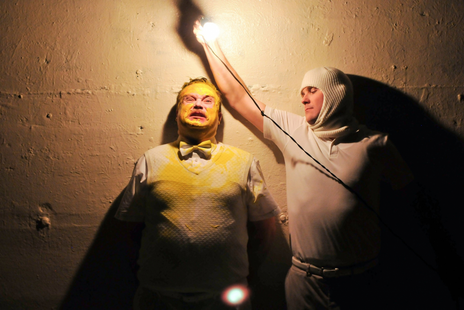 Actors, Edmund Lewis and Eric Tucker at a wall one with yellow paint on his face, the other holding a lightbulb