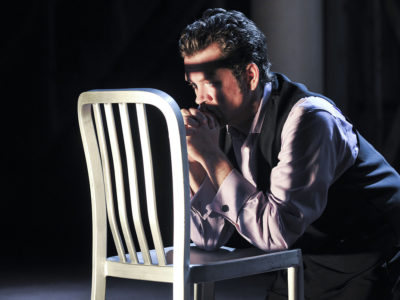 actor on stage kneeling at a chair in prayer pose